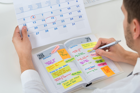 46637018 – close-up of businessman with calendar writing schedule in diary